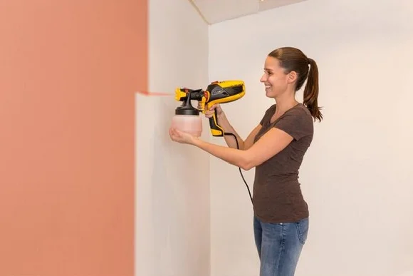 Person streicht Wand mit Farbspritzpistole